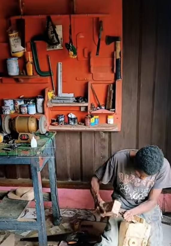 Emmanuel carving a mask in his workshop, in front of the orange tool wall